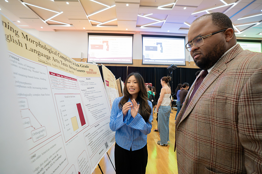 A man listens to a student present research from a poster.