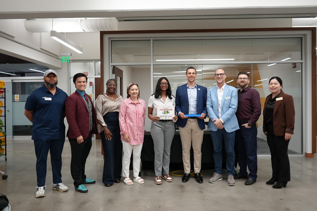 A group of nine people stands together in a modern office setting for a commemorative photo, with two individuals in the center holding an award certificate and a trophy.
