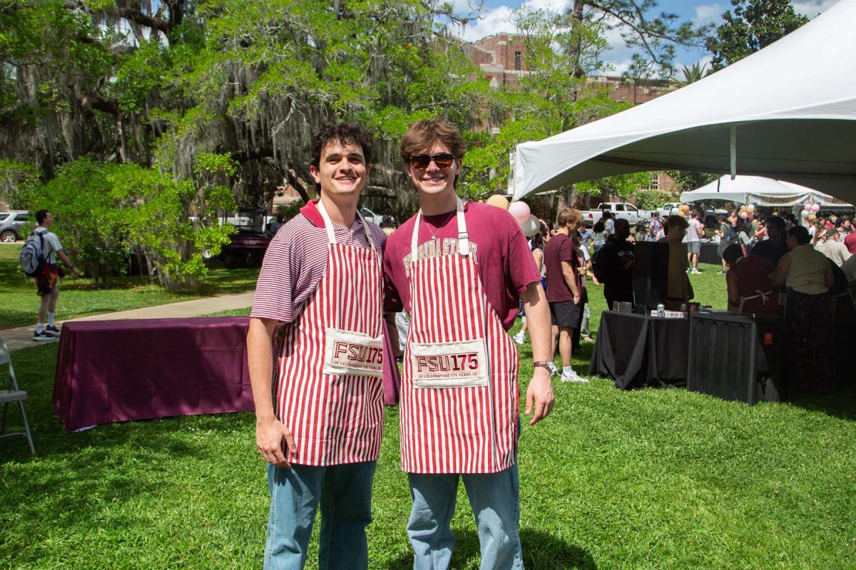 Two men smile and pose for a photo, both wearing red and white striped'FSU 175' aprons
