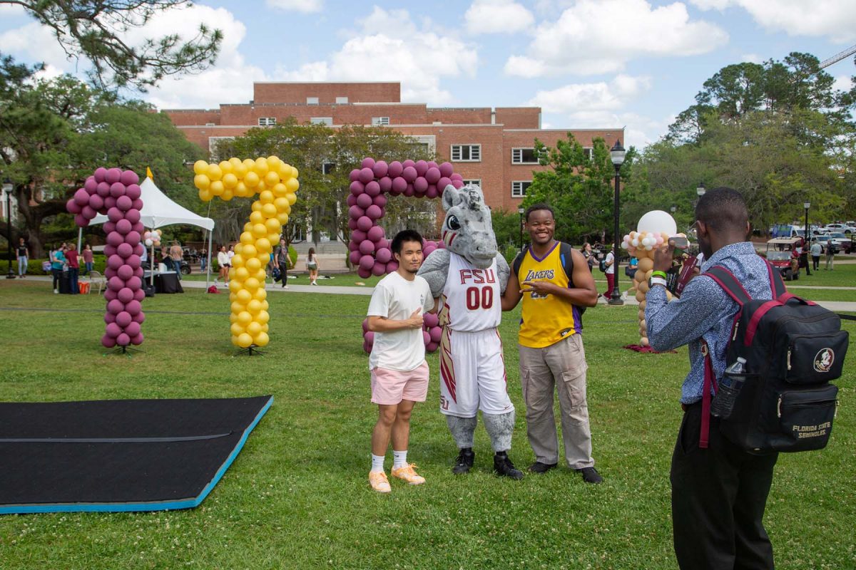 Two people pose for a picture with a mascot while someone takes the photo