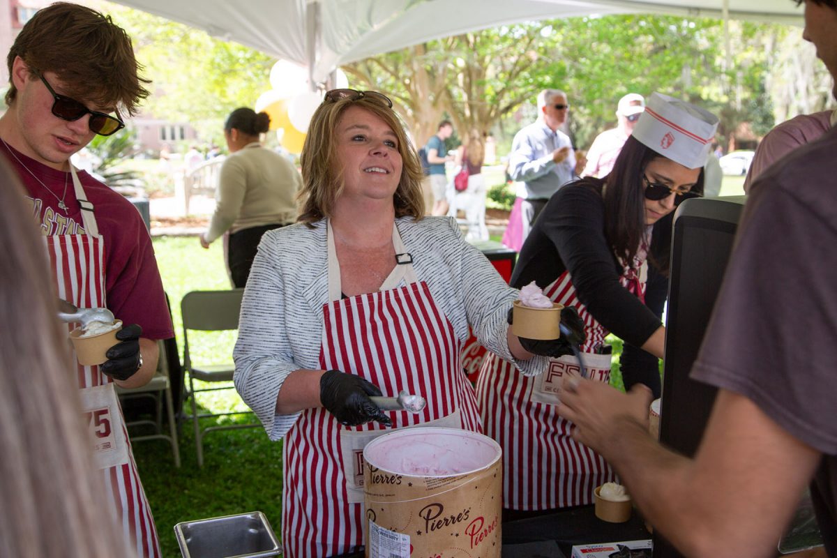 A woman wearing a red and white striped apron hands someone ice cream in a cup