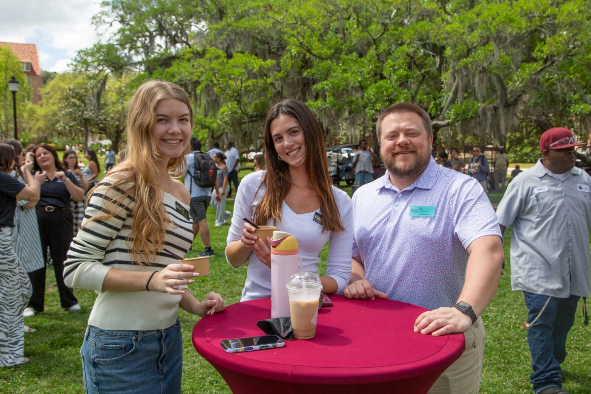 Three people smile, at a cocktail table, outside