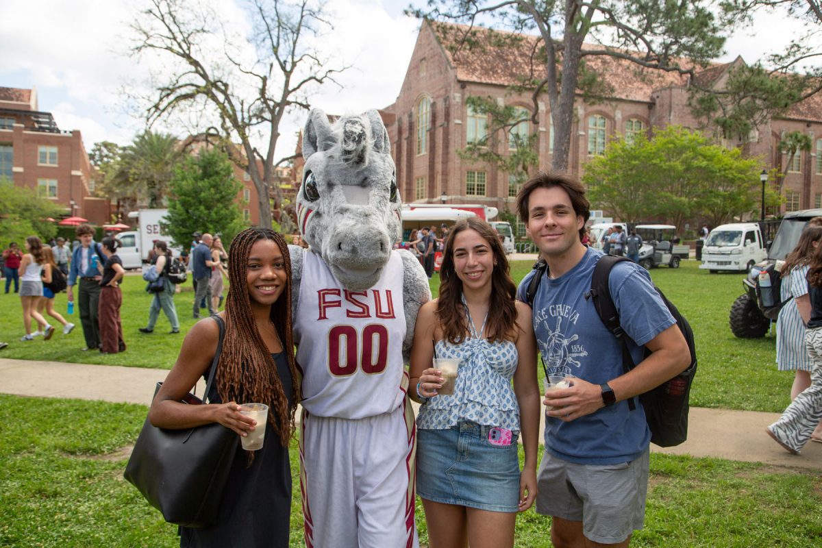 Three people smile with a mascot, outside