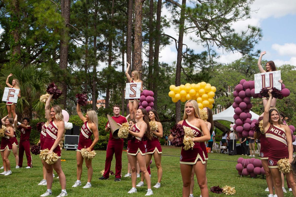 Cheerleaders outside, some with signs, and balloons in the back