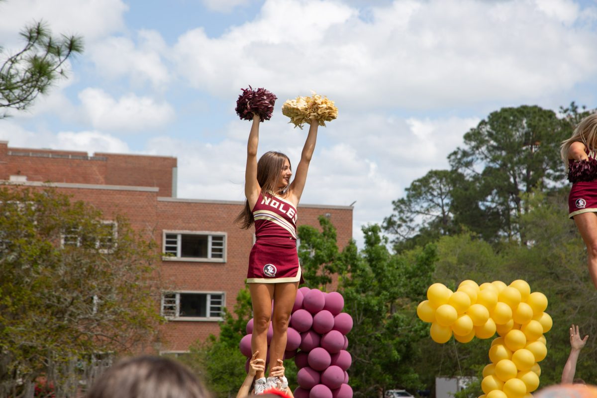 A cheerleader holds up her hands while she's held in the air by her ankles