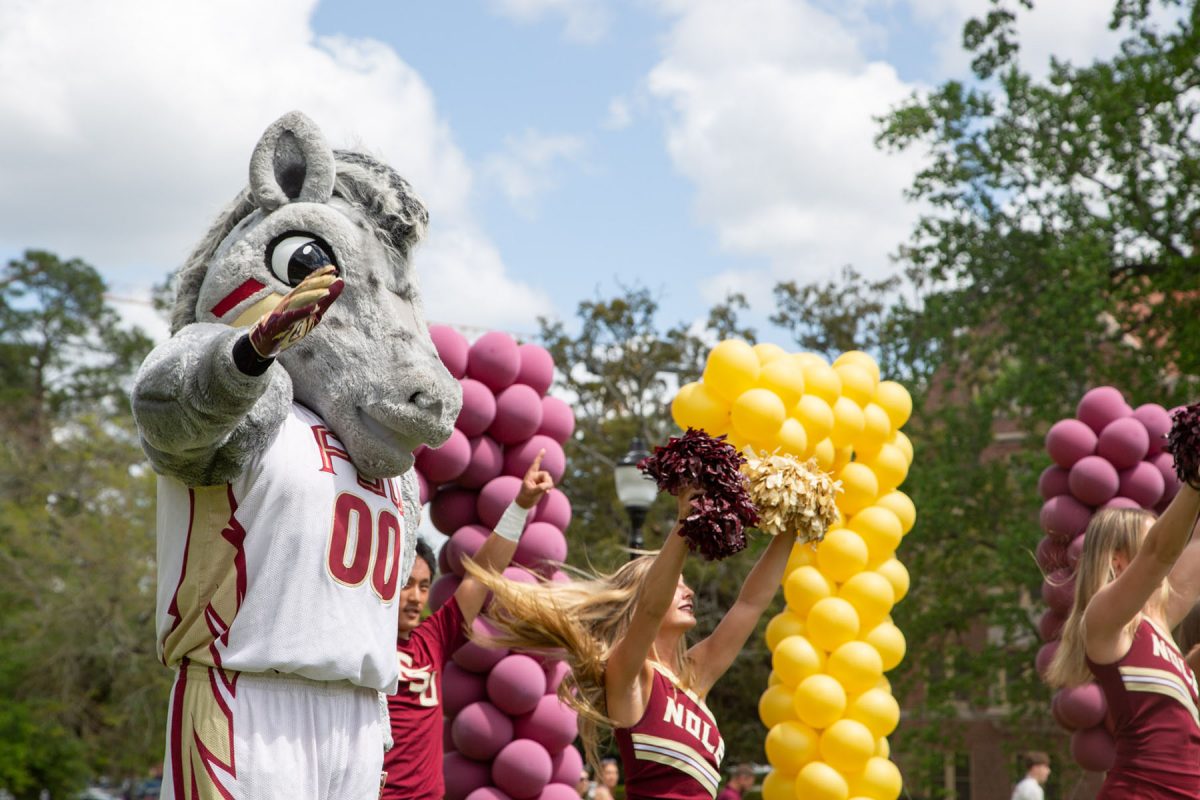 A mascot holds up his hand by cheerleaders and balloons, outside
