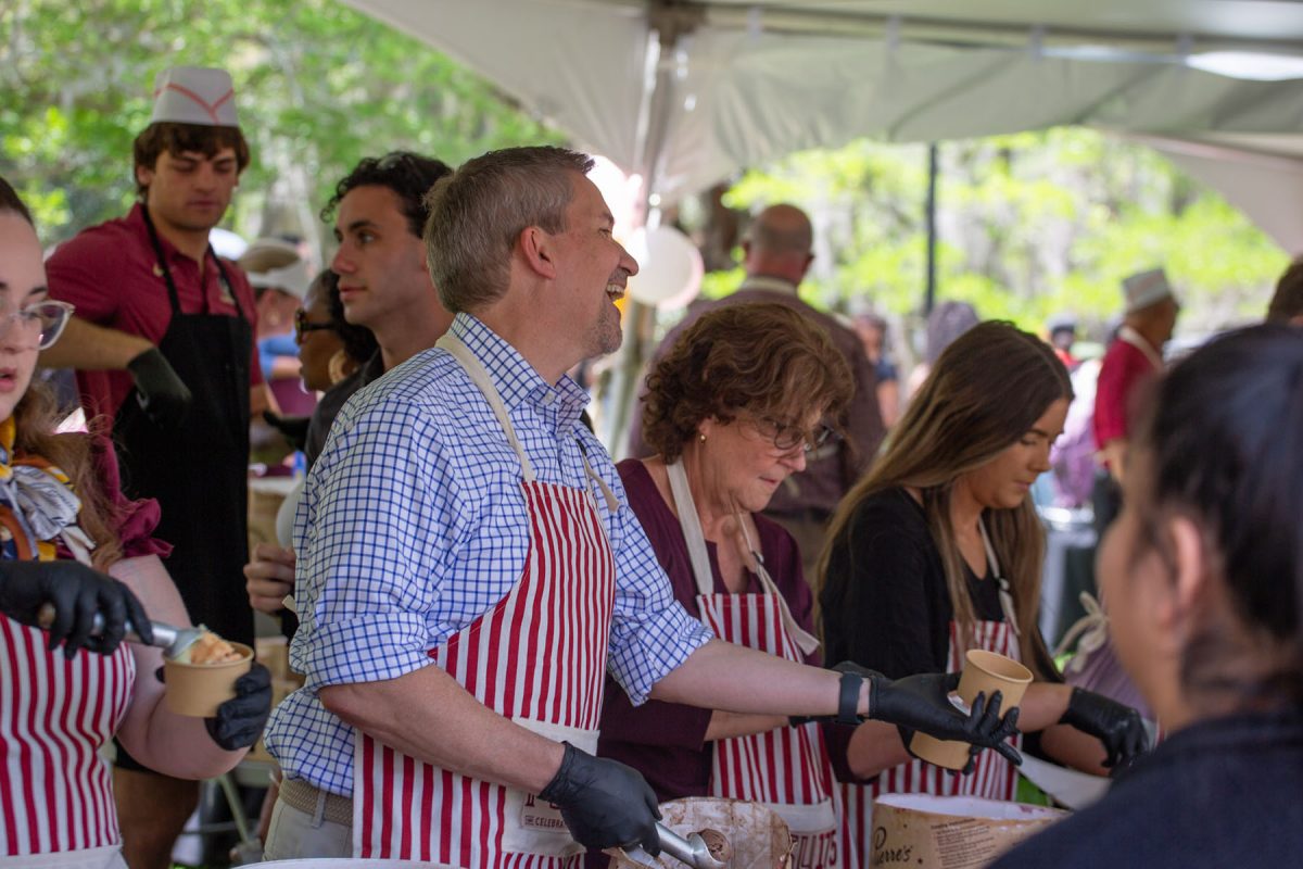 A man in a red and white striped apron, laughs holding a cup