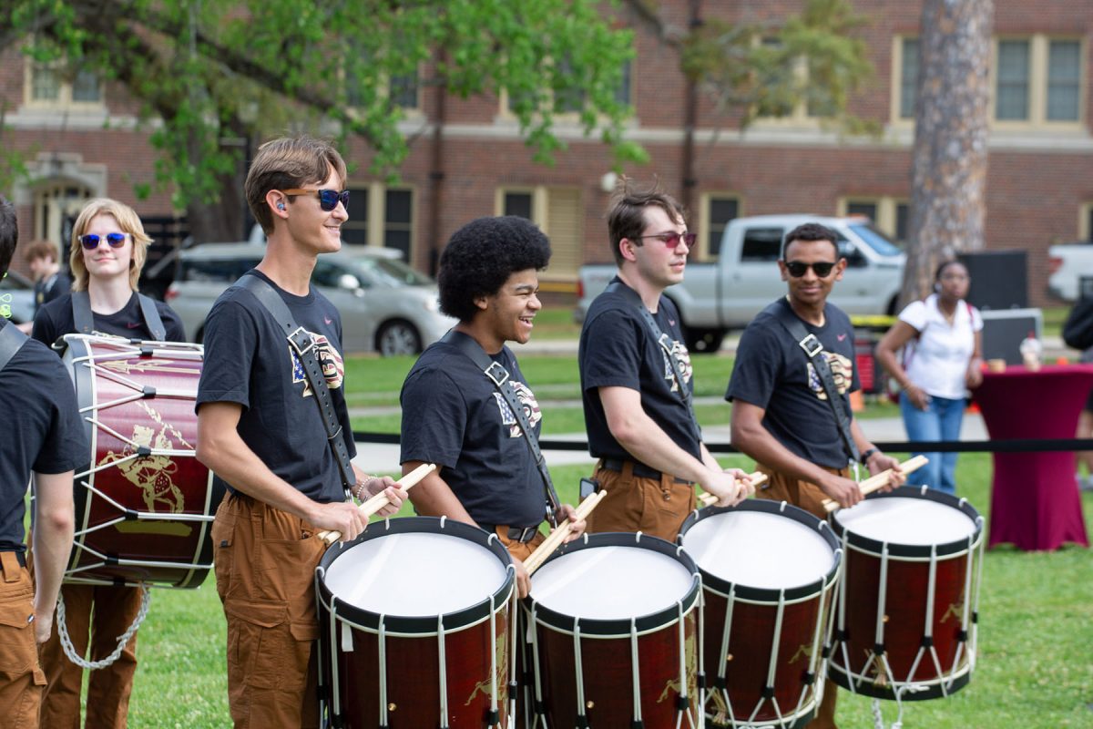 Students smile and hold their drumming sticks, with large drums strapped around their bodies