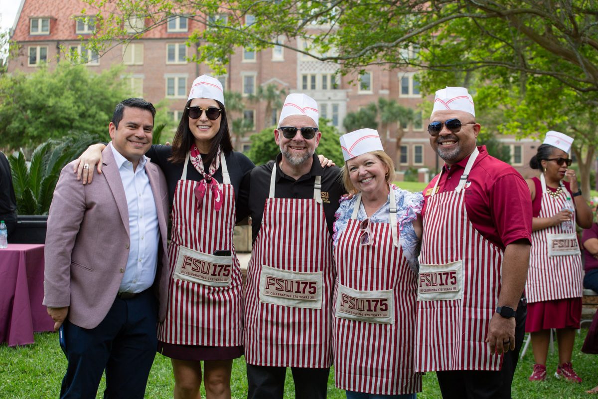 Five people smile for a photo, four of them wearing aprons and hats