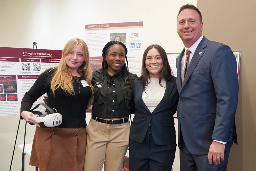 Four individuals standing in front of poster presentations at a conference.