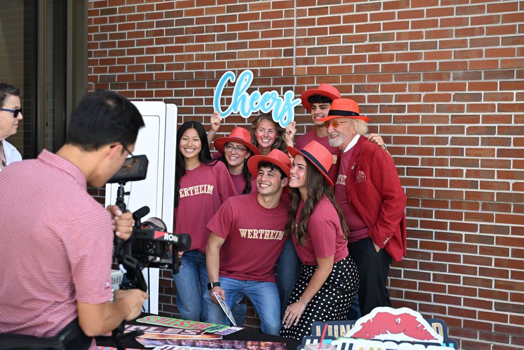 Dr. Herbert Wertheim poses with students who are holding a "cheers" photobooth sign.