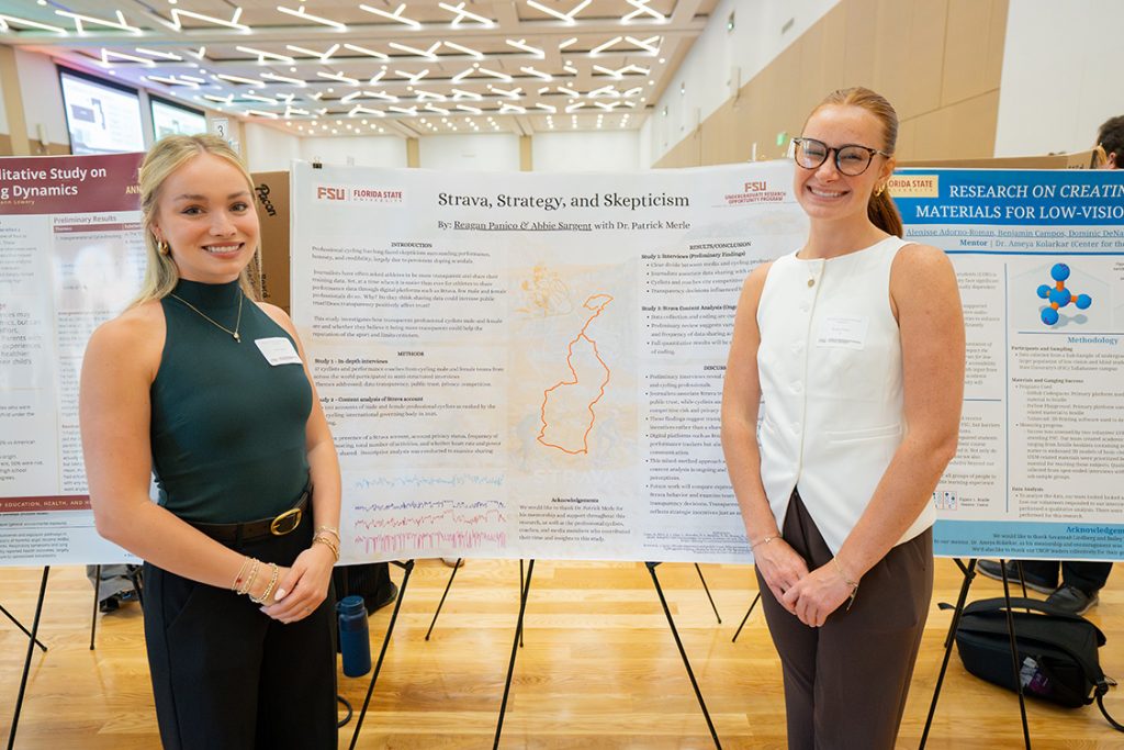 Two students stand in front of their research poster with the title "Strava, Strategy, and Skepticism."