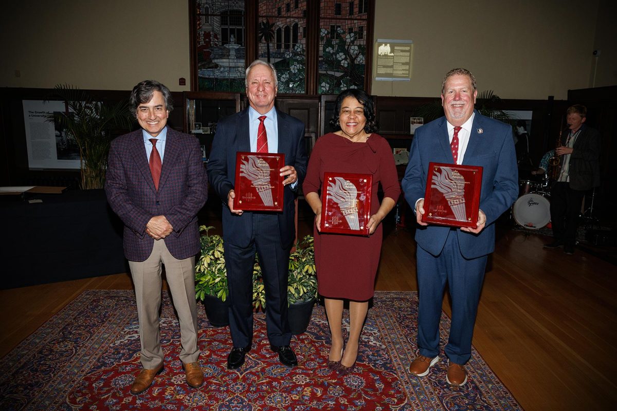 Three men in suits and a woman in a garnet dress hold plaques honoring them as Torch Award winners.