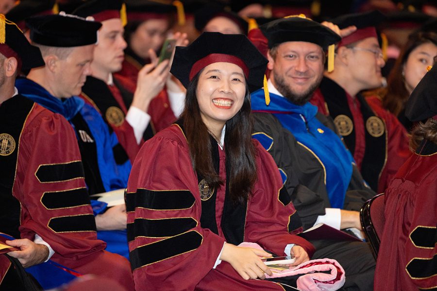 A female graduate wearing a garnet doctoral gown and black doctoral cap smiles for a photo.