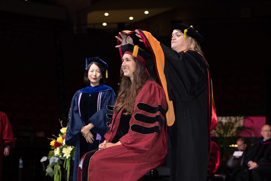 A female doctoral graduate is hooded by her female faculty mentor.