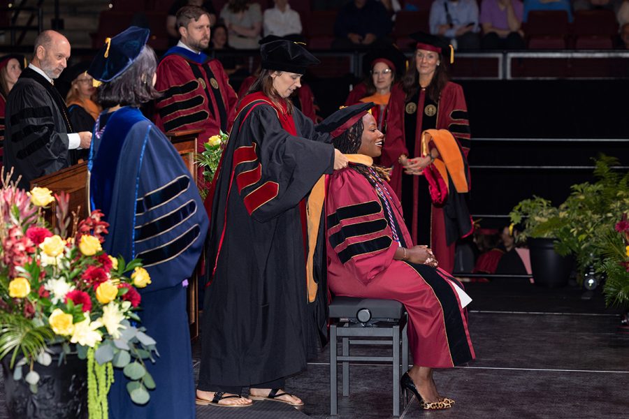 A black female doctoral graduate smiles as her faculty mentor places her doctoral hood.