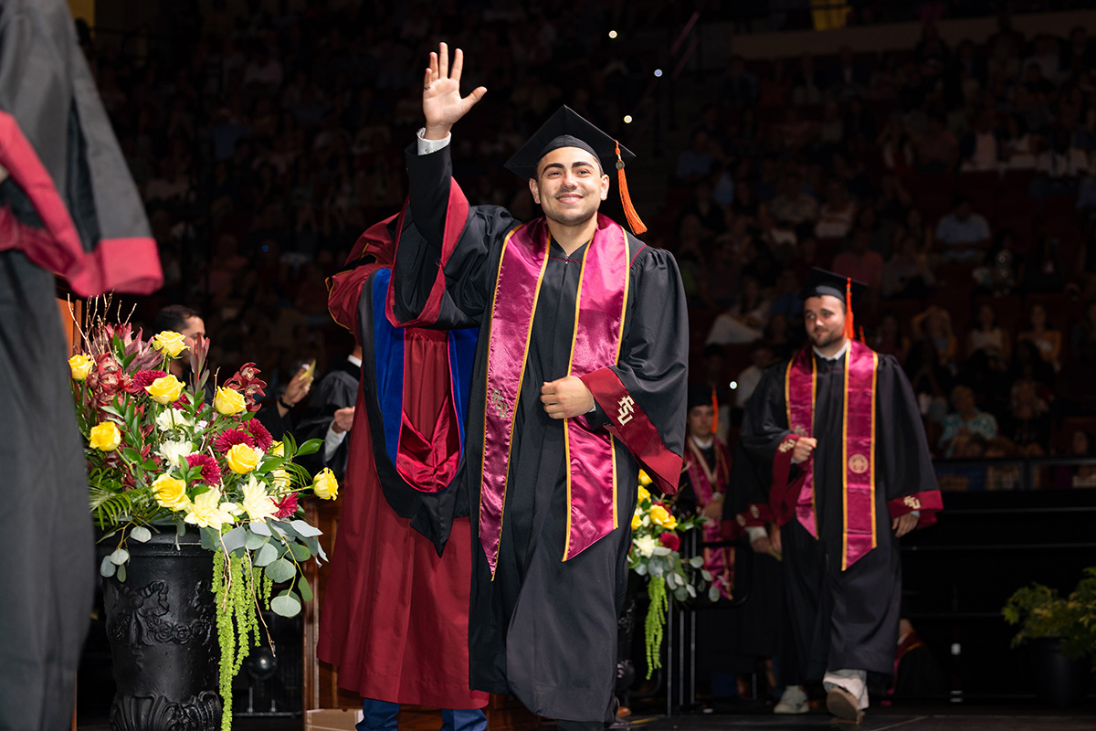 A graduate walks across the stage as faculty members stand nearby.