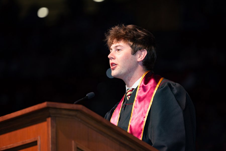 SGA President Carson Dale speaks into a microphone at a wooden lectern during a commencement ceremony.