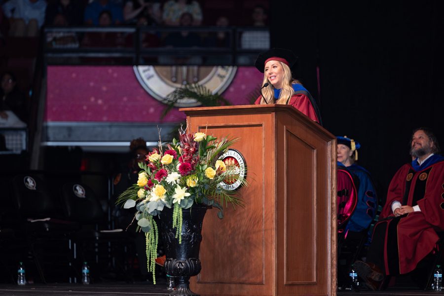 Sara Blakely addresses a large crowd from a wooden lectern during a commencement ceremony at Florida State University.