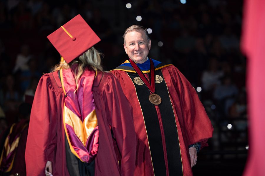 President McCullough stands on a stage and congratulates a graduating student during a commencement ceremony.