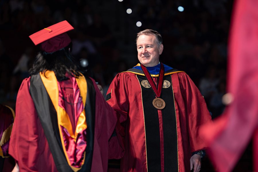 President Richard McCullough shakes hands with a graduating student on stage during a commencement ceremony.
