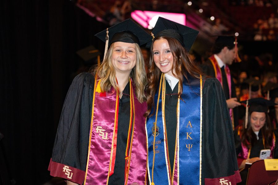 Two female graduates pose together at a Florida State University commencement ceremony, wearing black gowns with garnet trim and academic stoles.