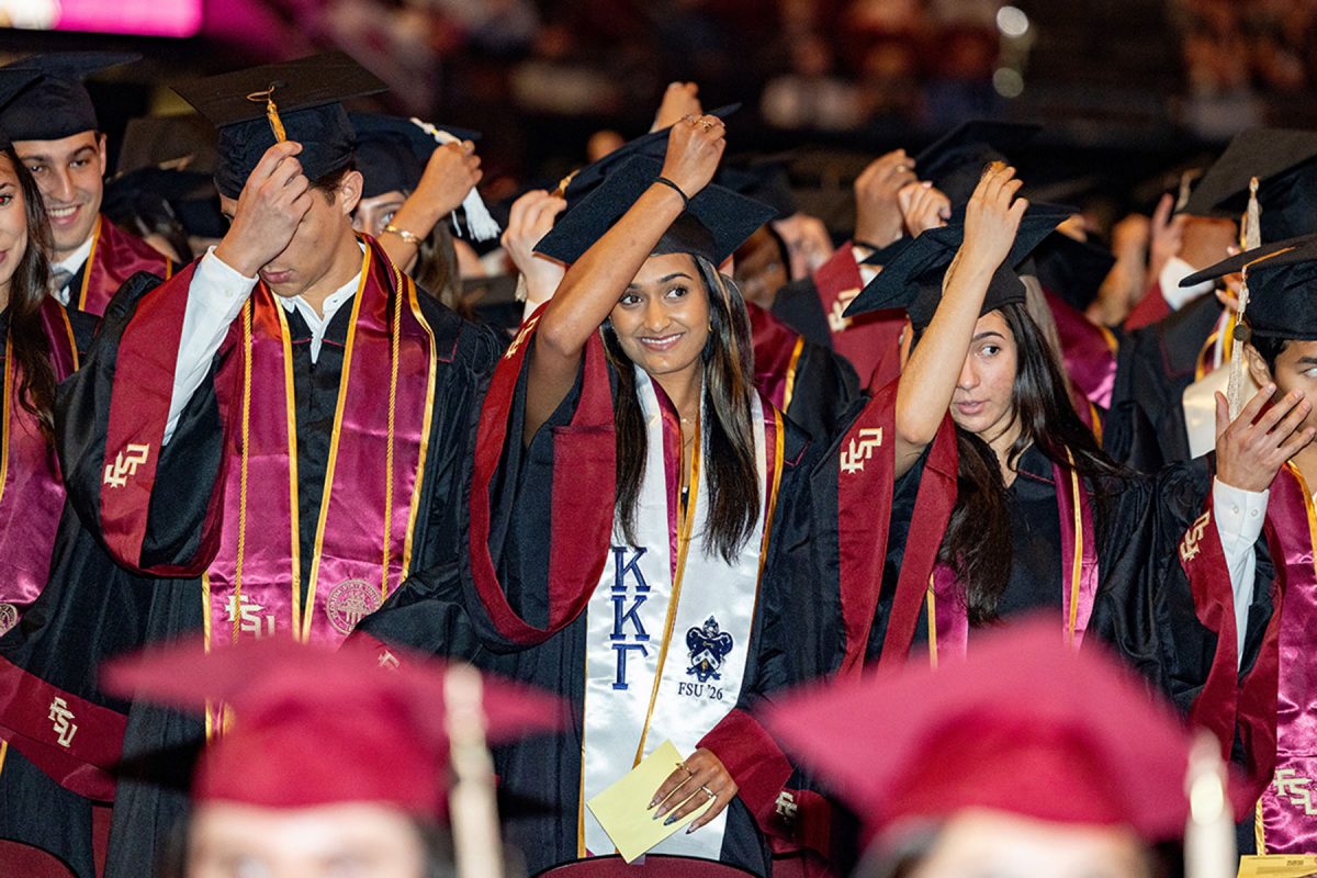 A group of graduates in garnet and black Florida State University regalia smile as they adjust their tassels during a commencement ceremony.