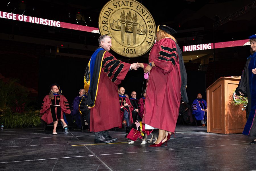 FSU President Richard McCullough shakes a black female doctoral graduate's hand as she walks her small black dog on stage.