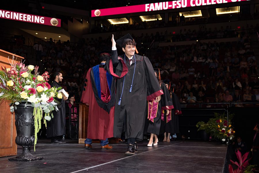 A student waves toward the audience while walking across the stage.
