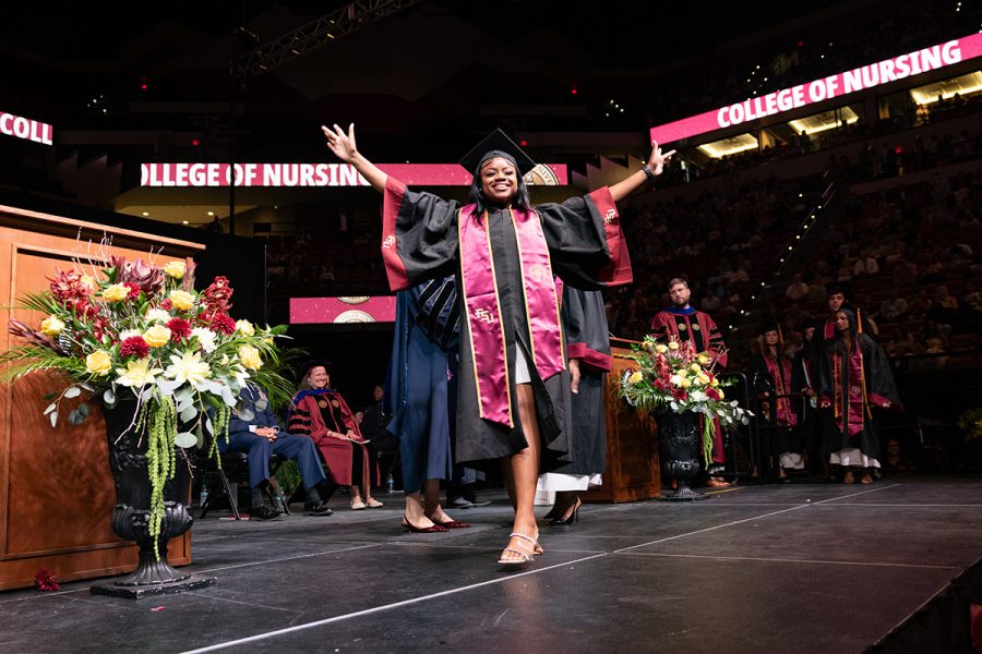 A graduate raises her arms in celebration while crossing the stage.