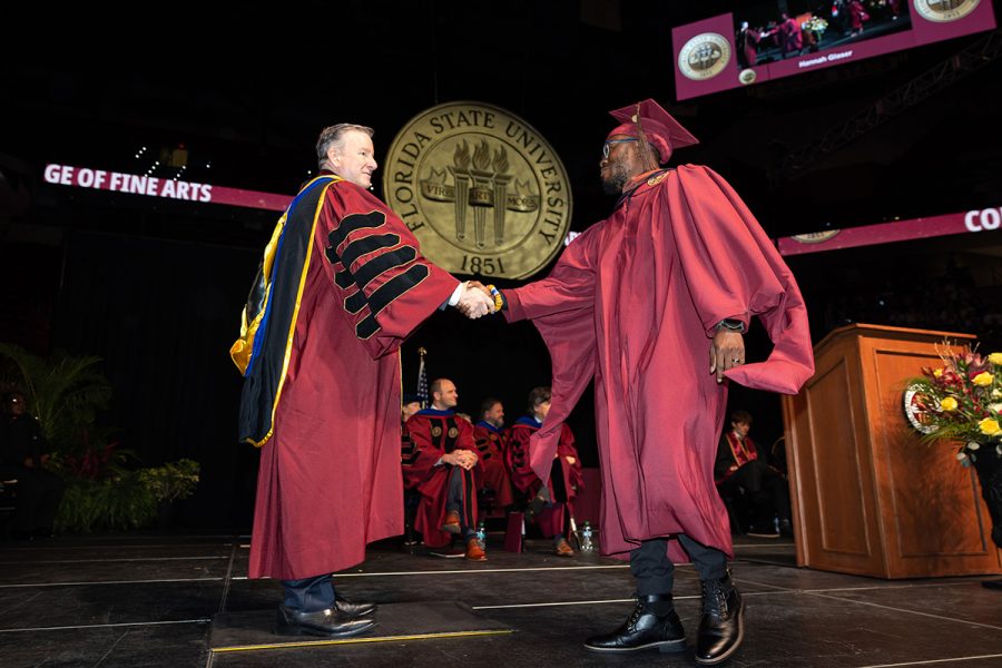 President Richard McCullough shakes hands with a graduate in garnet regalia on a stage featuring the Florida State University seal during a commencement ceremony.