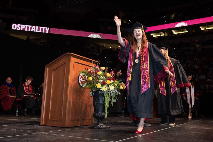 A graduate waves to the crowd while walking across the stage during commencement ceremony.