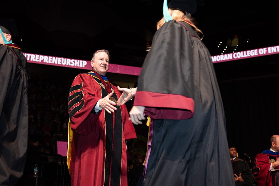 President Richard McCullough shakes hands with a graduate in a black and garnet gown on stage during a commencement ceremony.