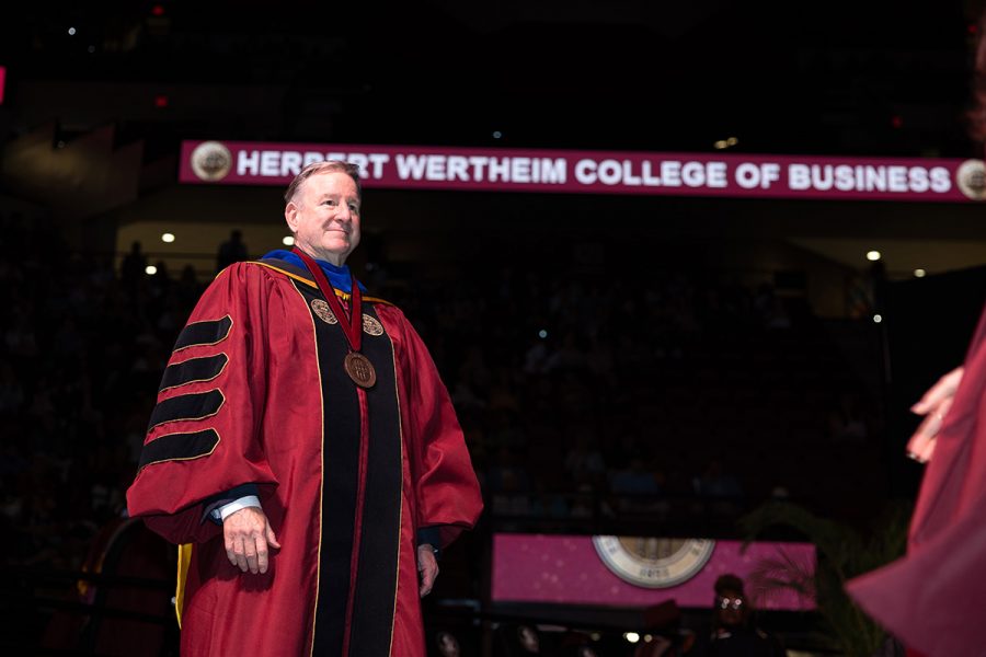 A graduate in a black gown and garnet stole smiles and points toward the crowd during a Florida State University commencement ceremony.