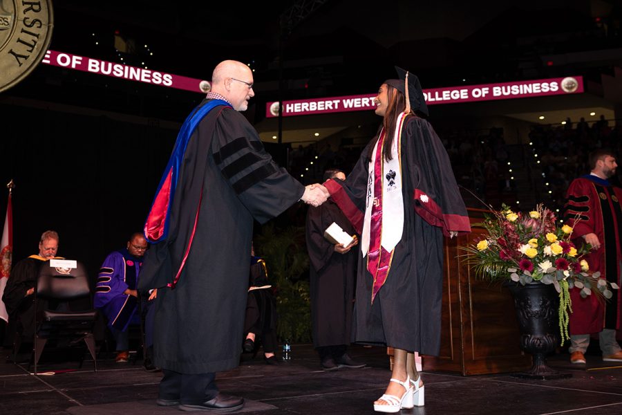Two graduates in black and garnet regalia smile for a selfie during a Florida State University commencement ceremony.