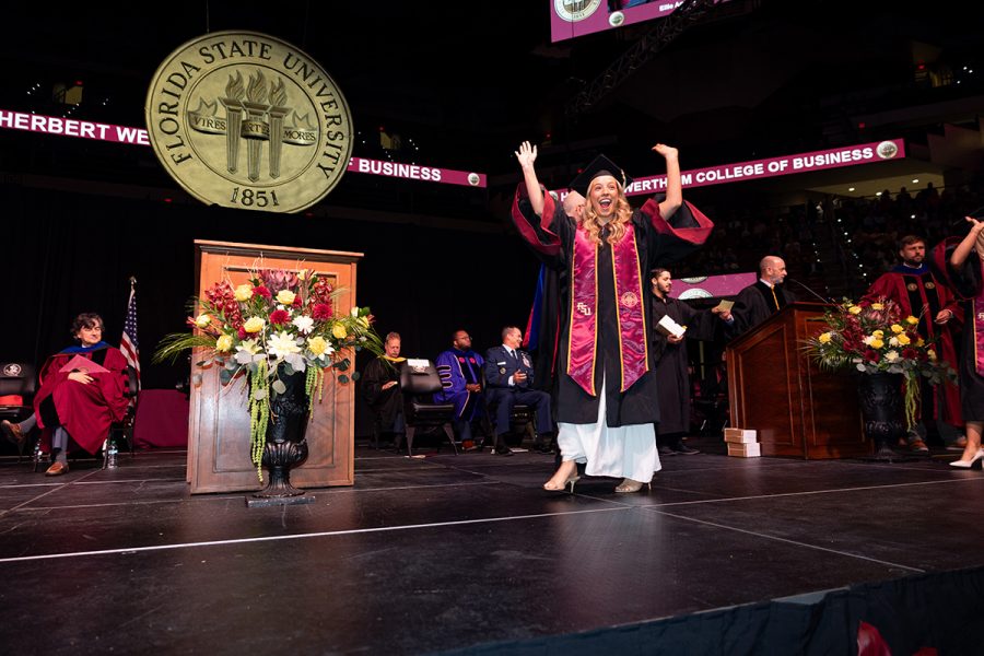 A graduate in a black cap and gown with a garnet and gold stole smiles for a photo at a Florida State University commencement ceremony.