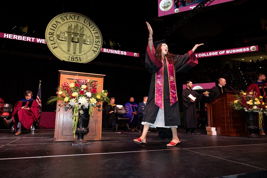 A jubilant Florida State University graduate celebrates with her arms raised on stage at the College of Business commencement ceremony.