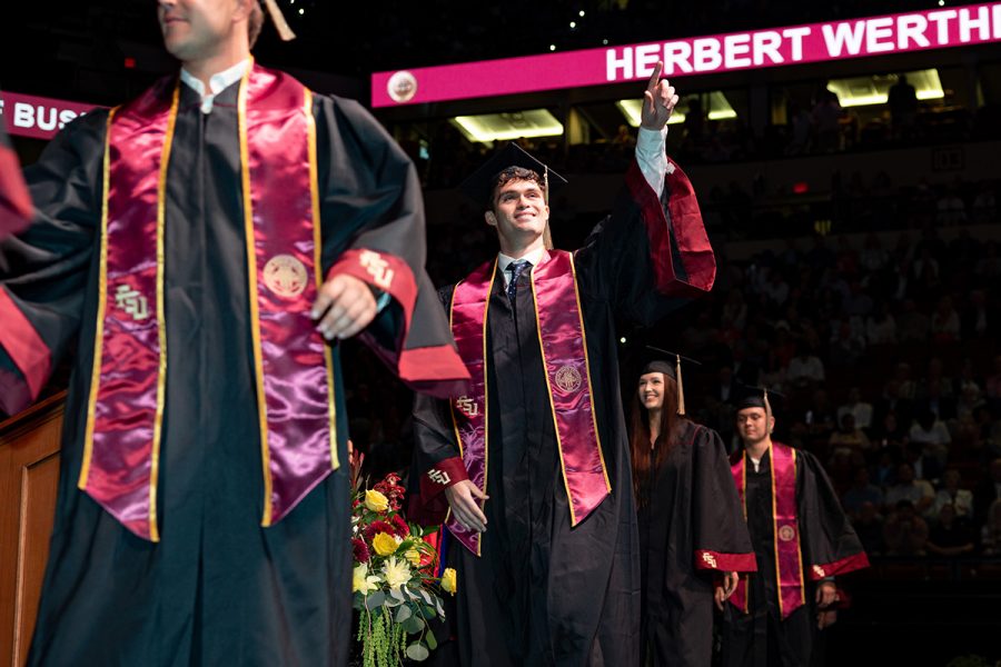 A graduate in a black cap and gown with a garnet stole celebrates and poses for a photo during a Florida State University commencement ceremony.