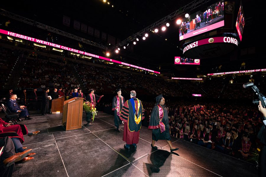 Graduates walk across the stage in garnet and black regalia during the Herbert Wertheim College of Business commencement ceremony at Florida State University.