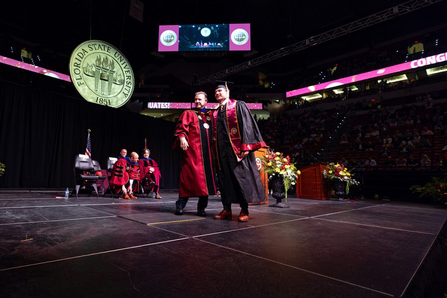 A Florida State University official in a garnet doctoral gown stands on stage with a graduate wearing a black gown and garnet stole.