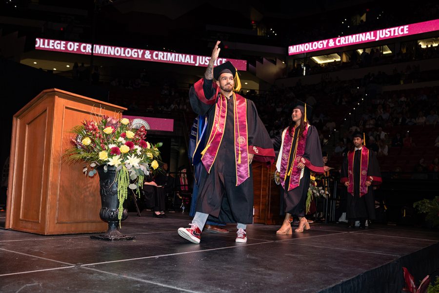 A graduate raises one hand while walking across the commencement stage.