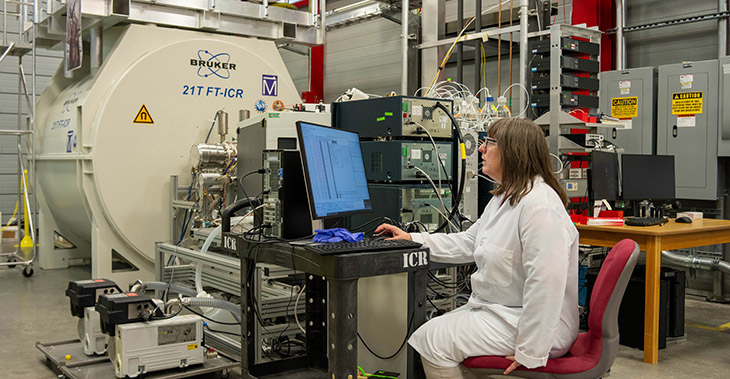 A woman sits at a computer terminal in front of scientific equipment.