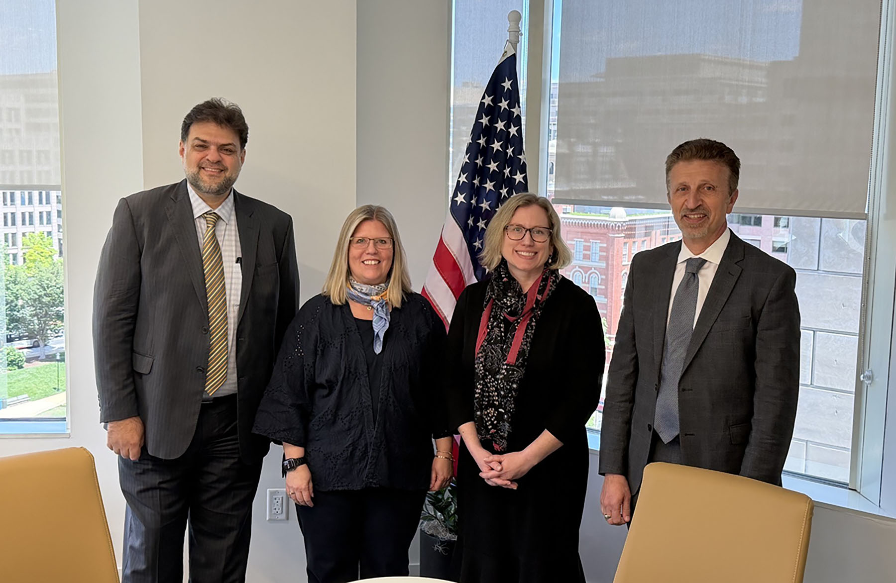 Four leaders stand together in a conference room following a partnership signing ceremony in Washington, D.C. From left are SI Director Rabieh Razzouk, IREX Chief Impact Officer Rebecca Bell Meszaros, LSI Associate Director Stephanie Simmons Zuilkowski and IREX President and CEO Aleksander Dardeli. An American flag is visible behind them near large windows overlooking the city.