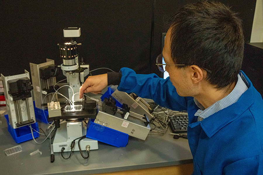 A man in a blue lab coat works with a small microscope grid.