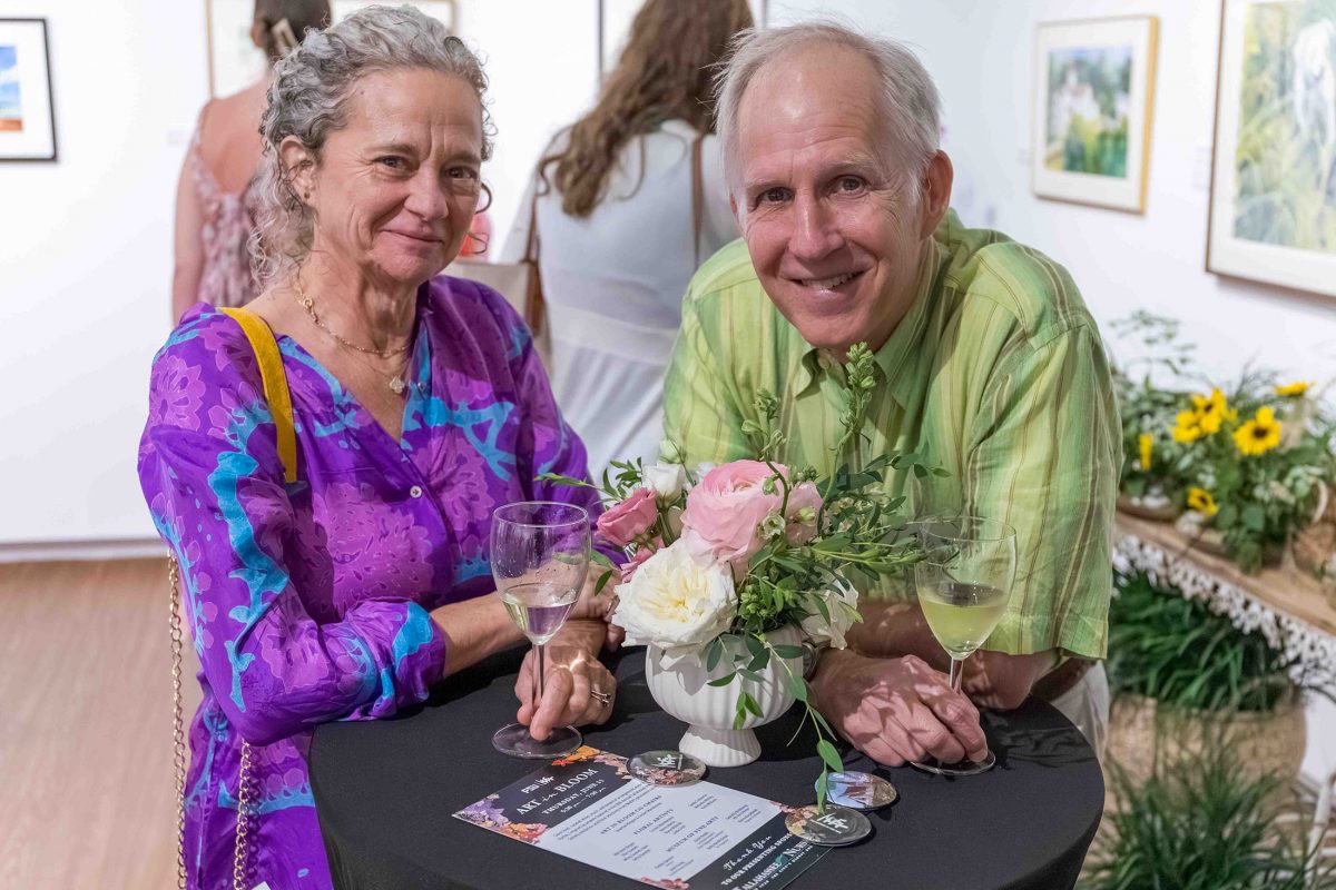 A man in woman standing at a high-top table smile for a photo.