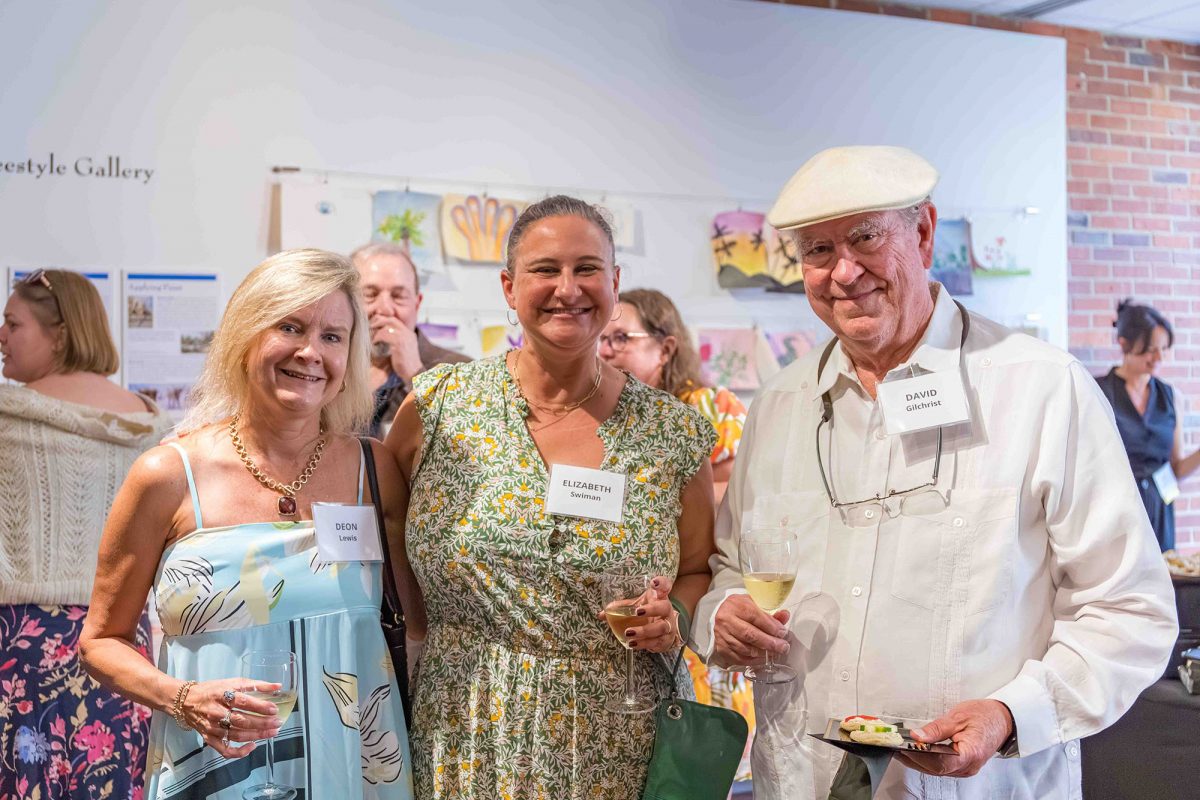 Two women and a man holding drinks smile for a photo at the Art in Bloom event