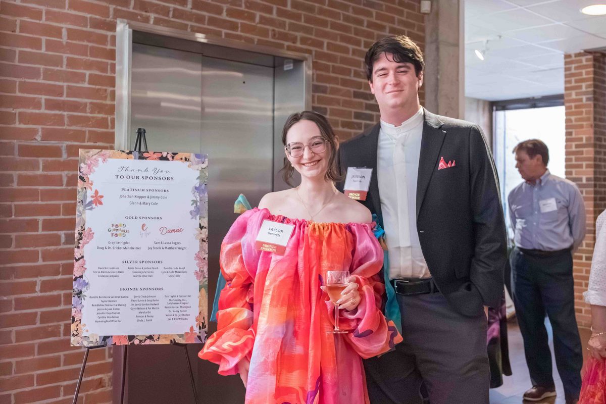 A young man and woman smile next to a sponsors poster at the Art in Bloom event.