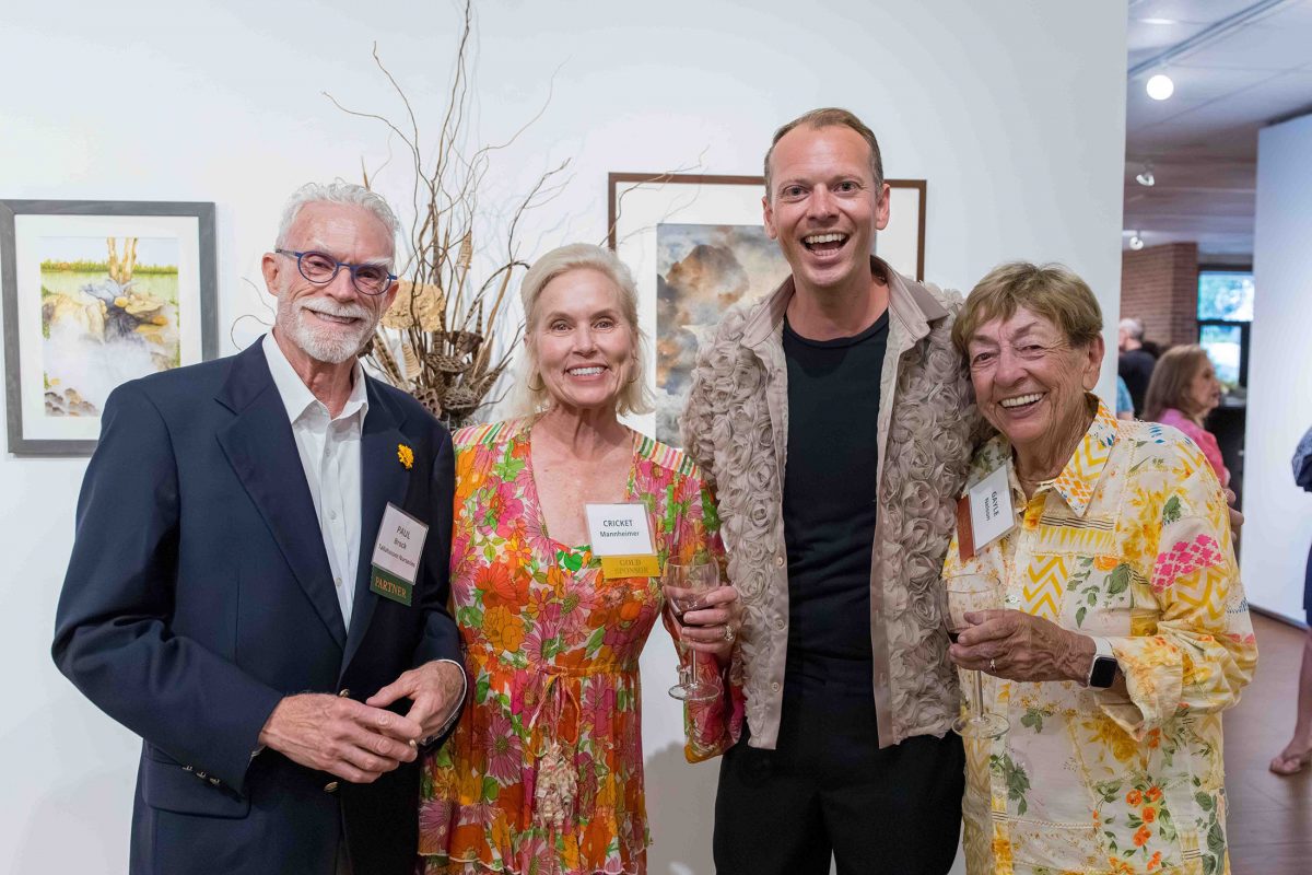 Four people stand in front of art for a group photo