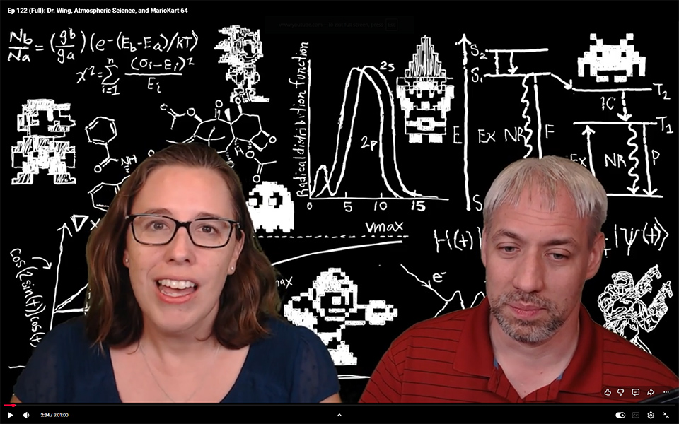 A YouTube screenshot with black and white math and science sketches in the background and two people talking in the foreground.