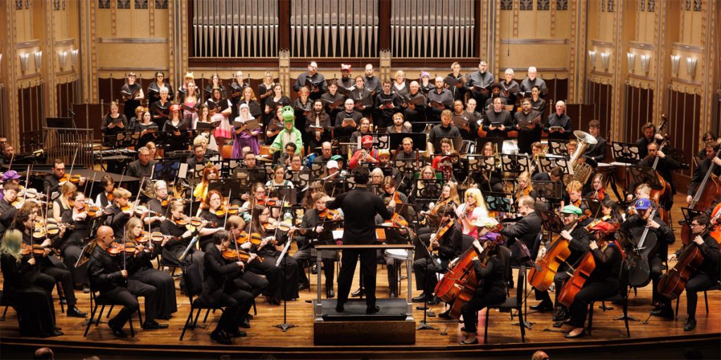An orchestral ensemble plays in a concert hall. Some of the musicians and singers are dressed as popular video game characters.